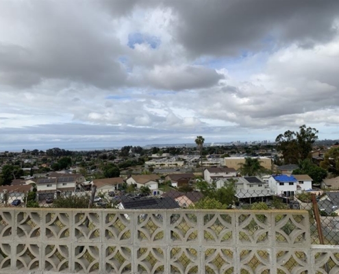 1ae005c2-05dc-42a4-a0d4-d34cfd7c800a Cloudy sky over a peaceful suburban neighborhood with houses, trees, and a decorative concrete wall in the foreground.