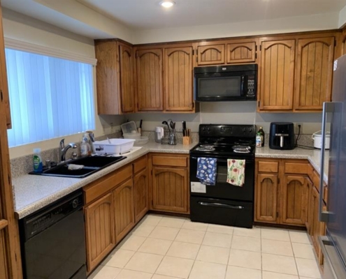 32941546-679a-491d-a106-c0133641eae9 Kitchen with wooden cabinets, black appliances, sleek gray countertops, and modern utensils on the counters.