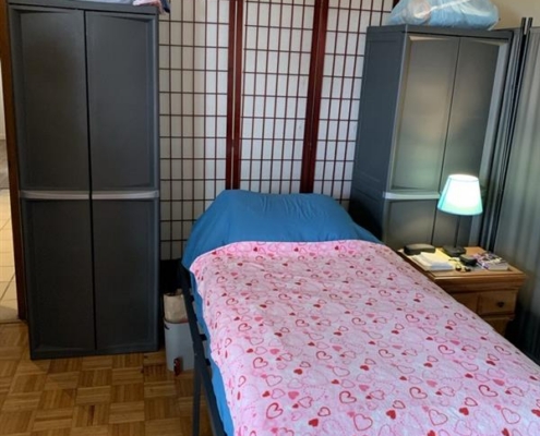 bc0cce54-10aa-4cb1-87da-9093b9655d31 Single bed with a pink heart-patterned blanket, two tall cabinets, and a lamp on a small white bedside table for added charm.