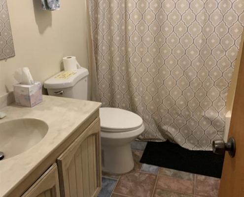 dc260971-2ae5-4733-bdaa-834b9ad42176 Small bathroom with a patterned shower curtain, modern toilet, sink with cabinet, and tiled floor.